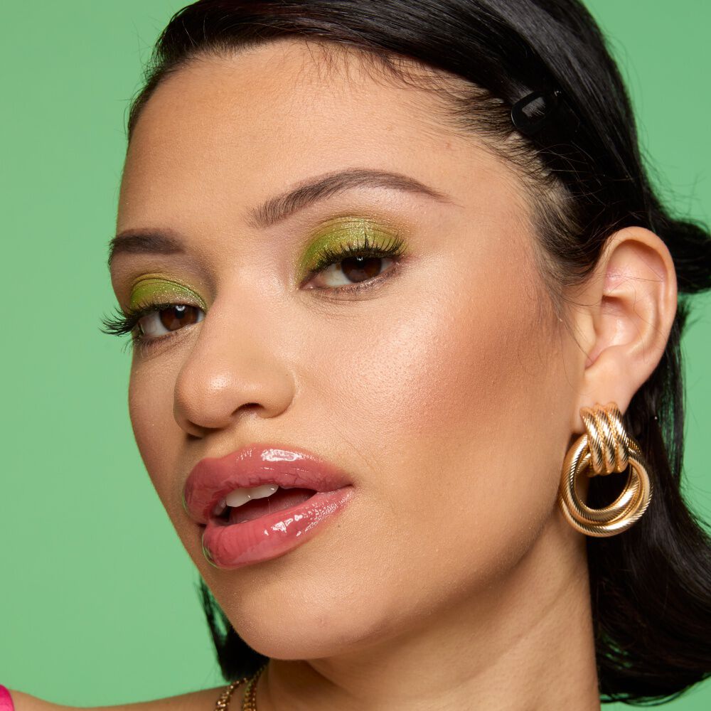 Gesicht einer Frau mit leicht geoffneten Mund, der mit glossy Lipgloss geschminkt ist vor grunem Hintergrund