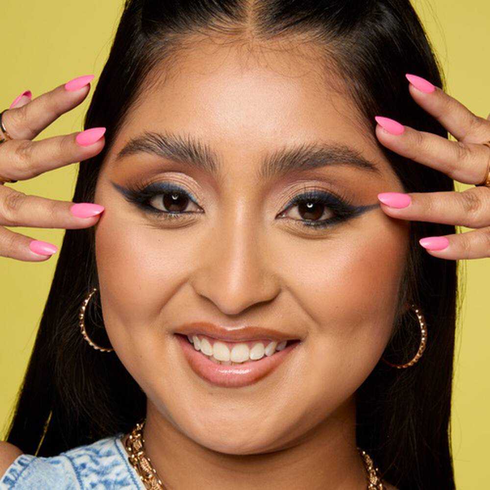 Lachelnde brunette Frau vor einem gelben Hintergrund, die sich ihre Hande an die Schlafen halt