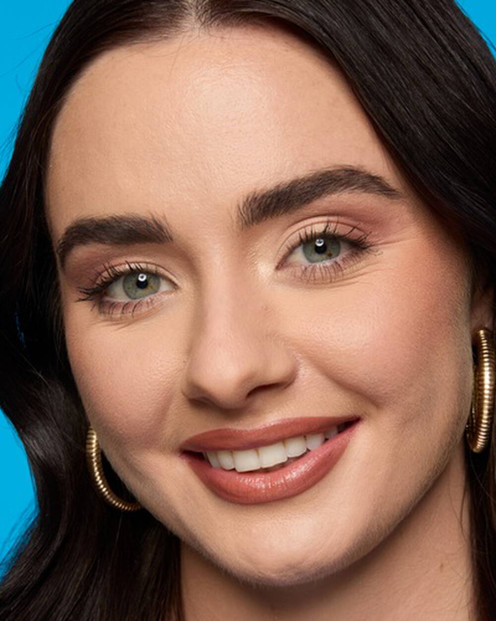 Lachelnde Frau mit braunen Haaren und schonen Augenbrauen vor einem turkisen Hintergrund