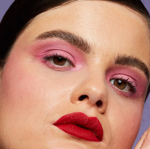 Junge Frau mit hellem Hautton, perfekt gestylten Augenbrauen, rosa Lidschatten und roten Lippen