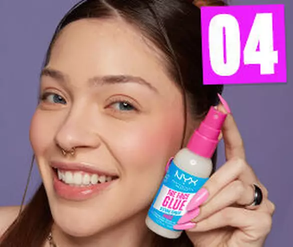 Junge Frau zeigt lachelnd einen Flakon NYX „The Fast Glue“ vor einem lilafarbenen Hintergrund.