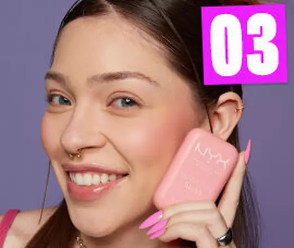 Eine junge Frau lachelt, halt einen pinken NYX Blush in der Hand, mit auffalligen Nageln vor einem lila Hintergrund.