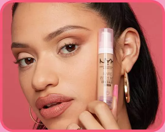 Model mit ebenmaßigen Teint halt das feuchtigkeitsspendende NYX Bare With Me Concealer Serum neben ihr Gesicht.