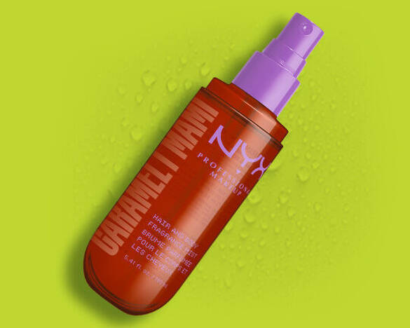 Die orangefarbene Spruhflasche des NYX Caramelt Mami Hair and Body Fragrance Mists vor einem grunen Hintergrund mit Wassertropfen.