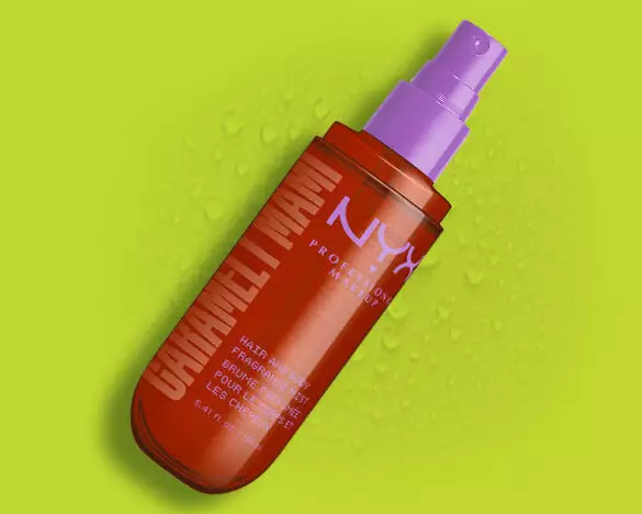 Die orangefarbene Spruhflasche des NYX Caramelt Mami Hair and Body Fragrance Mists vor einem grunen Hintergrund mit Wassertropfen.