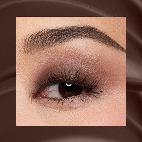 Close-up of an eye area with NYX Professional Makeup Lid Lingerie Cream Eye Pigment in 06 Mocha Mesh, shown on a brown mate textured background.