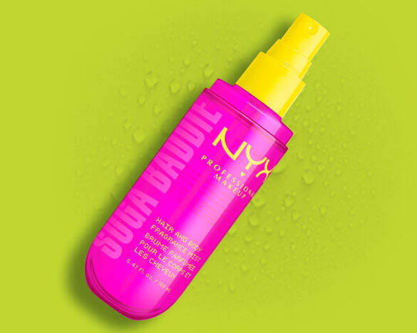 Das NYX Hair and Body Fragrance Mist „Suga Baddie“ in einer pinken Spruhflasche, umgeben von frischen Wassertropfen.