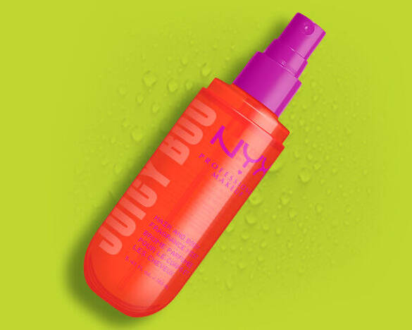 Das orangefarbene NYX Juicy Boo Hair and Body Fragrance Mist mit purpurnem Spruhkopf vor einem grunen Hintergrund.