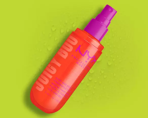 Das orangefarbene NYX Juicy Boo Hair and Body Fragrance Mist mit purpurnem Spruhkopf vor einem grunen Hintergrund.