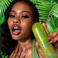 Ein Model prasentiert das Coconut Cutie Fragrance Mist vor einem tropischen Hintergrund aus grunen Palmblattern.