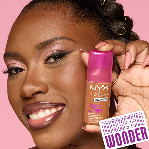 Nahaufnahme einer jungen, lachelnden Frau, die die Make 'Em Wonder Foundation in die Kamera halt