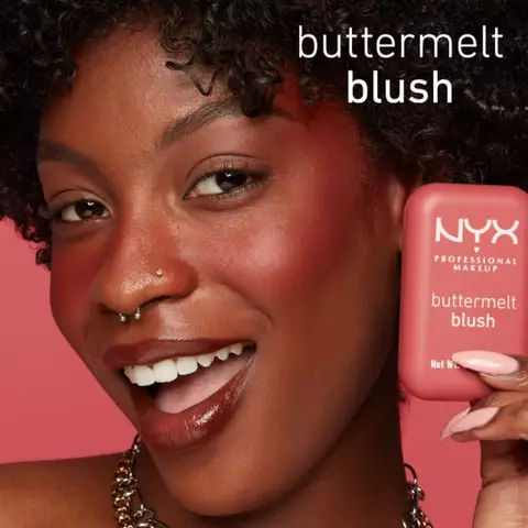 Lachelnde Frau, die den NYX Buttermelt Blush neben ihr Gesicht halt