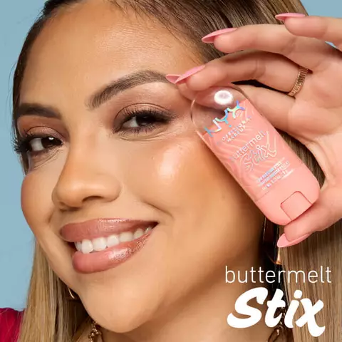 Gesicht einer Frau, die lachelnd den Buttermelt Highlighter Stix an ihre linke Schlafe halt