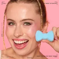 Eine lachelnde Frau halt das hellblaue Maggie Simpson Make-up-Schwammchen neben ihr Gesicht.